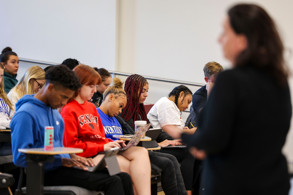 An instructor stands in front of a class full of seated students. 