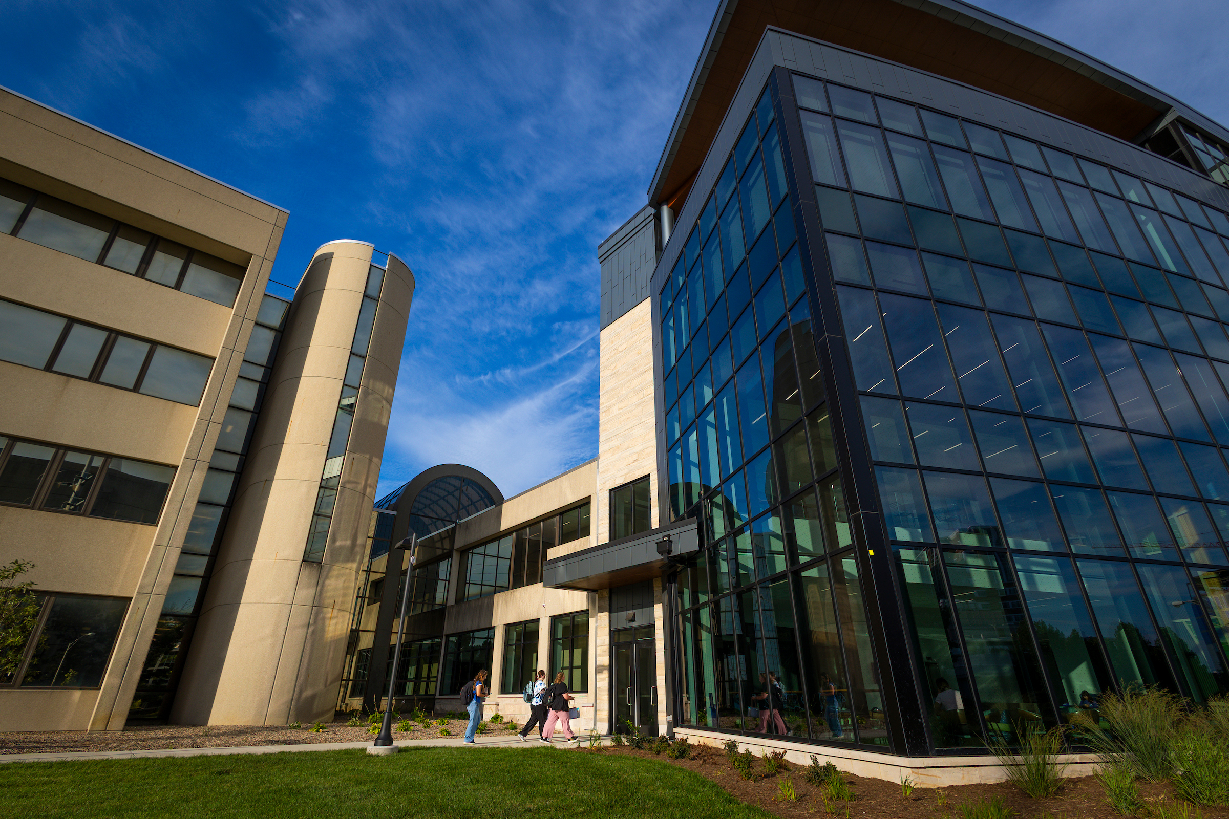 A large glass and concrete building with students entering and exiting. 
