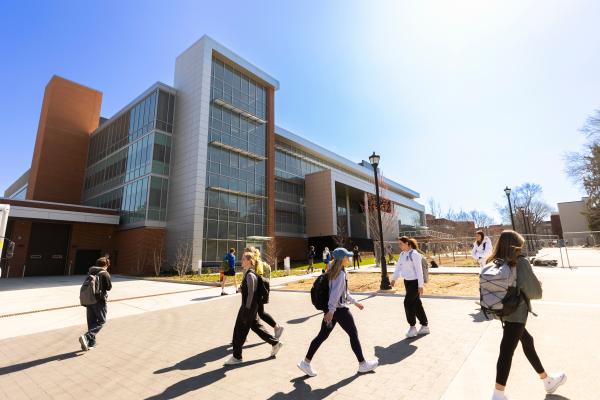 students walking past a glass front building on a bright and sunny day with fairly clear skies