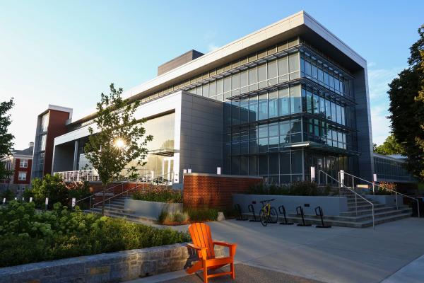 Glass-fronted building in the background set against a blue sky with some shrubbery and an orange Adirondack chair in the foreground.