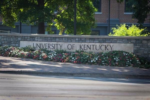 A low stone wall with "University of Kentucky" etched into it and some flowers in planted in front of it.