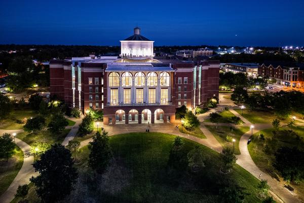 William T. Young Library lit up at night from an aerial view with a dark blue sky in the background.