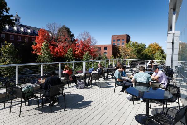 a rooftop patio of students studying at tables with fall leaves and buildings in the background