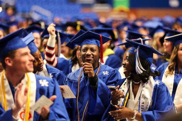 A crowd of students in UK blue graduation gowns and mortarboards are seated in Rupp Arena.