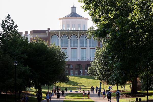 A large library in the background with a peaked dome and students walking in the foreground on sidewalks on a sunny day.