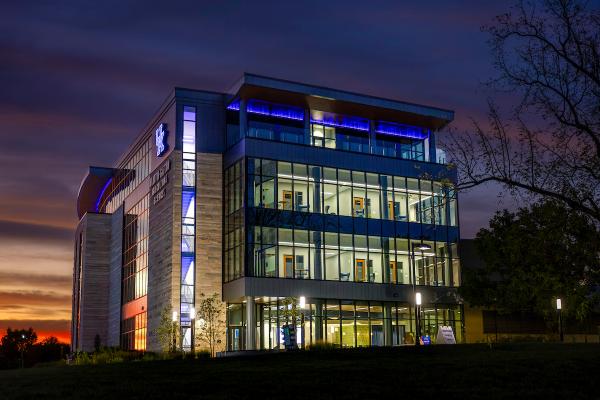 A four-story stone and glass building seen at dusk with hallways and offices visible from outside.