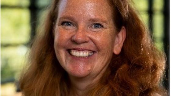 headshot of woman with red hair smiling wearing a printed purple blouse with a neutral sweater overtop. 