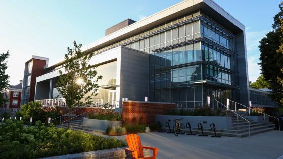 Glass-fronted building in the background set against a blue sky with some shrubbery and an orange Adirondack chair in the foreground.