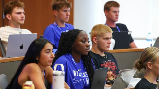 students sitting in tiered rows with laptops and water bottles set up in front of them