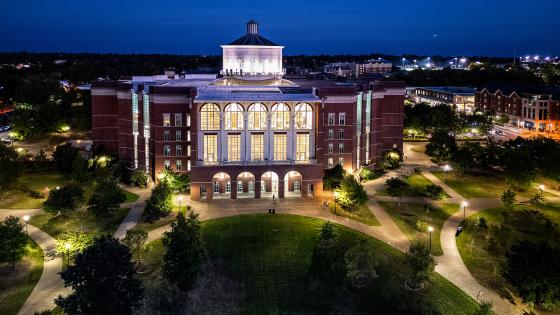 William T. Young Library lit up at night from an aerial view with a dark blue sky in the background.