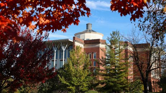 William T. Young Library framed by red and orange foliage with a blue sky in the background