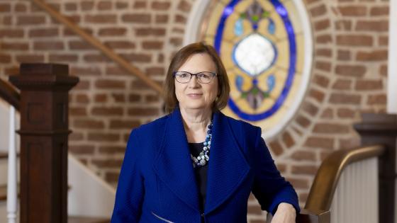 Laura Stephenson in a blue blazer poses next to a chair and stairs