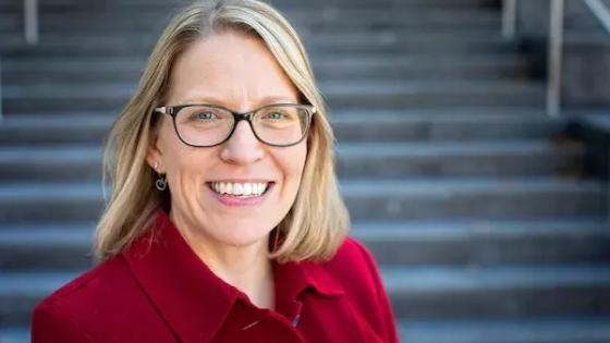 Headshot of Melissa Henke in a red shirt in front of steps.