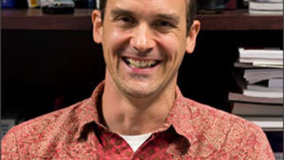 Headshot of Rick Ingram in a red-orange collared shirt.