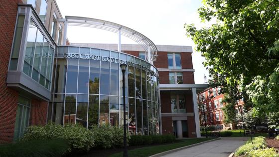 The front of the Gatton College of Business and Economics at UK, with a wall of windows looking into the atrium and greenery lining the sidewalk outside.
