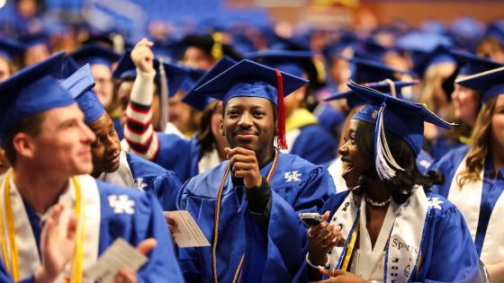 A crowd of students in UK blue graduation gowns and mortarboards are seated in Rupp Arena.