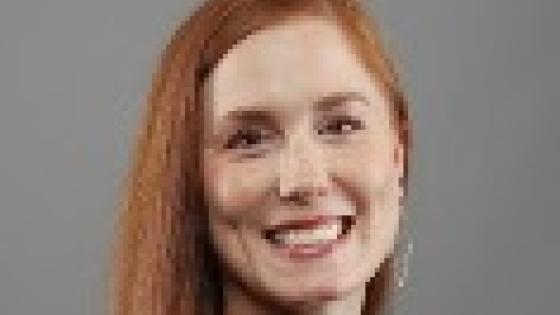 a woman with red hair posing for a headshot wearing a black blouse against a gray background