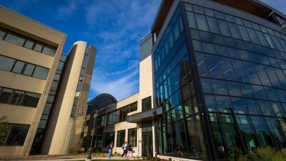 A large glass and concrete building with students entering and exiting. 
