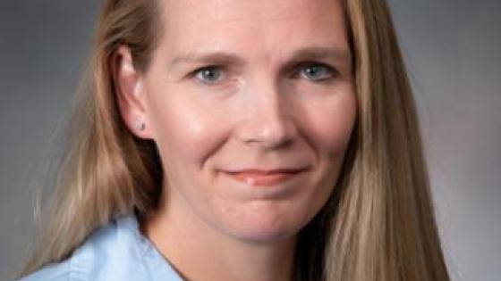 Jill Clemons posing for a headshot wearing a light blue collared shirt against a gray background. 