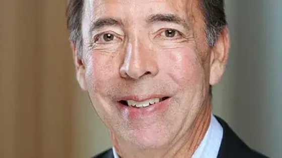 Jon Chait posing for a headshot wearing a light blue button down and black blazer.