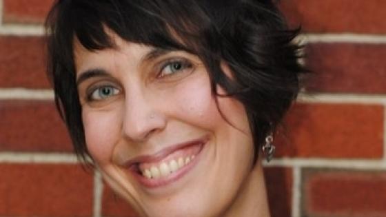 Woman with short brown hair smiling and posing against a brick wall
