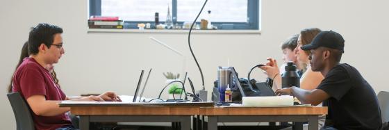 Side view of students sitting at a table looking at their laptops.