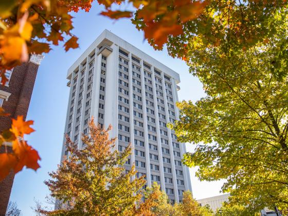 A tall, white concrete building framed by trees and orange leaves in the fall.