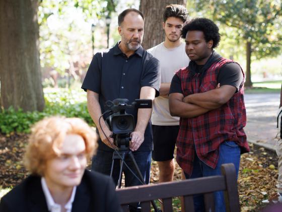 a man showing two students how to use a large camera to film an interview outdoors