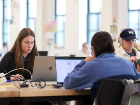 students sitting at a wooden table looking at their laptops