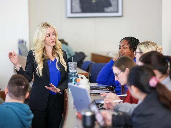 an instructor in front of a desk of students explaining with her hands