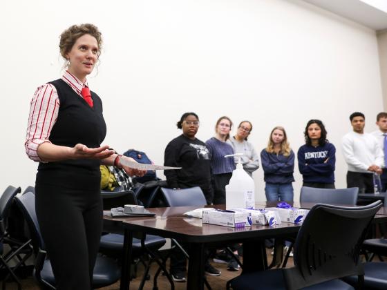 a teacher in front of a group of students with a piece of paper and nitrile gloves on a table
