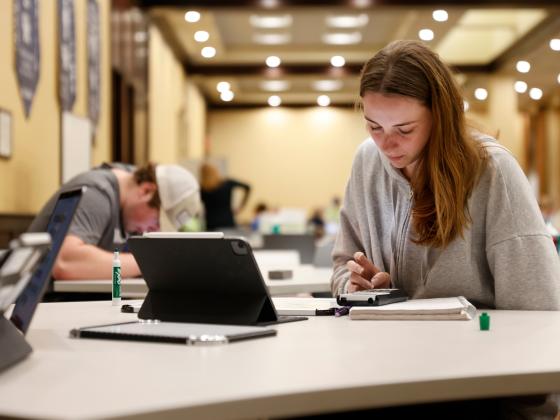 a student at a table wearing a gray sweatshirt and looking at an iPad and notebook