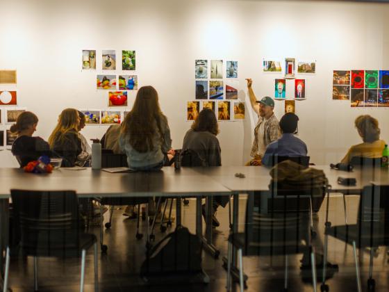 group of students in photo class sitting at one side of a table looking toward a gallery wall