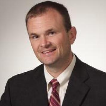 Headshot of Matt Bacon in a suit and red striped tie.