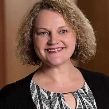 Headshot of Holly Hapke in a black cardigan and patterned shirt.