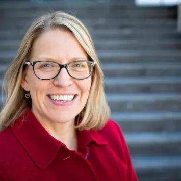 Headshot of Melissa Henke in a red shirt in front of steps.