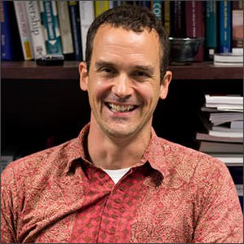 Headshot of Rick Ingram in a red-orange collared shirt.