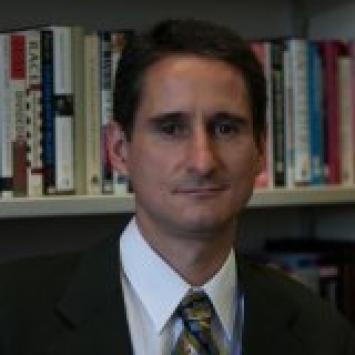 Headshot of Steve Voss in a suit in front of a bookshelf.