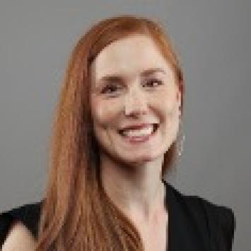 a woman with red hair posing for a headshot wearing a black blouse against a gray background