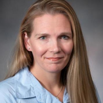 Jill Clemons posing for a headshot wearing a light blue collared shirt against a gray background. 