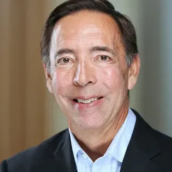 Jon Chait posing for a headshot wearing a light blue button down and black blazer.