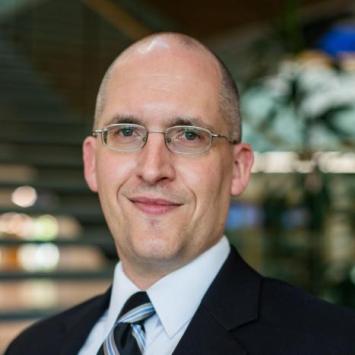Nathan Vanderford posing for headshot, wearing a black suit and tie and glasses