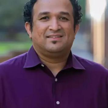 Savio Poovathingal posing for a headshot while wearing a plum button down.