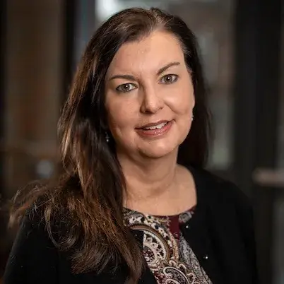 Headshot of woman with brown hair wearing black sweater and patterned shirt.