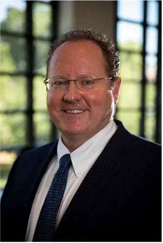 Headshot of man with eye glasses wearing a black suit, white shirt and blue tie