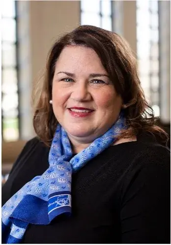 Headshot of woman with short brown hair wearing a black shirt with a royal blue neck scarf.