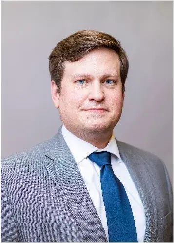 Headshot of male with short, brown hair wearing a gray suit with a blue tie and white button-up shirt. 