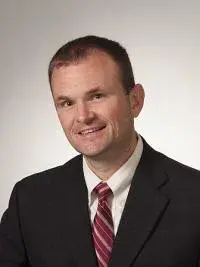 Headshot of Matt Bacon in a suit and red striped tie.