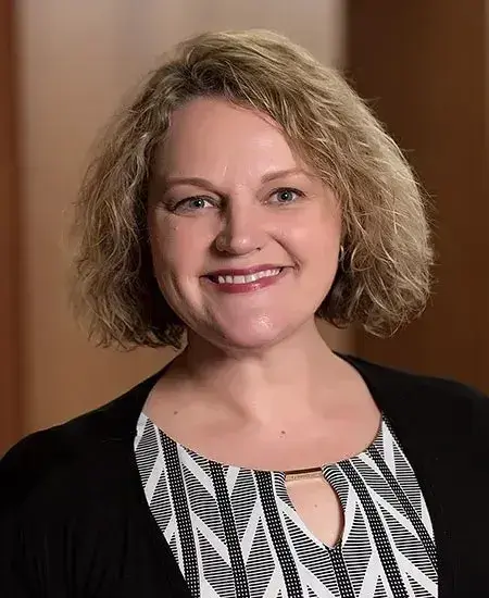 Headshot of Holly Hapke in a black cardigan and patterned shirt.