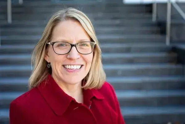 Headshot of Melissa Henke in a red shirt in front of steps.